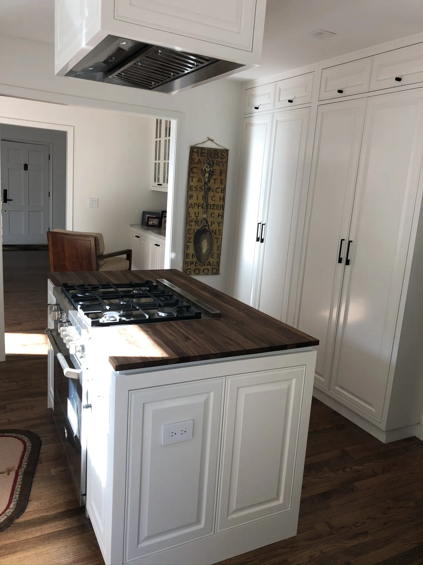Kitchen with white upper cabinets, gray island, black gas range, and pendant lighting