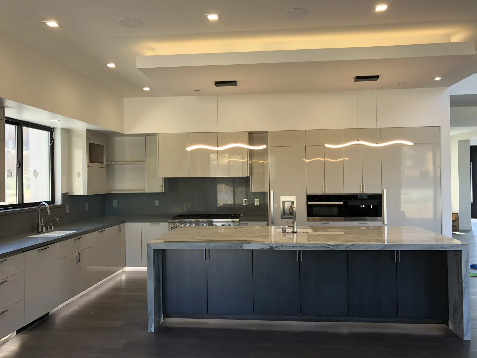 Modern kitchen with cream and white glossy cabinets, gray tile backsplash, and dark island