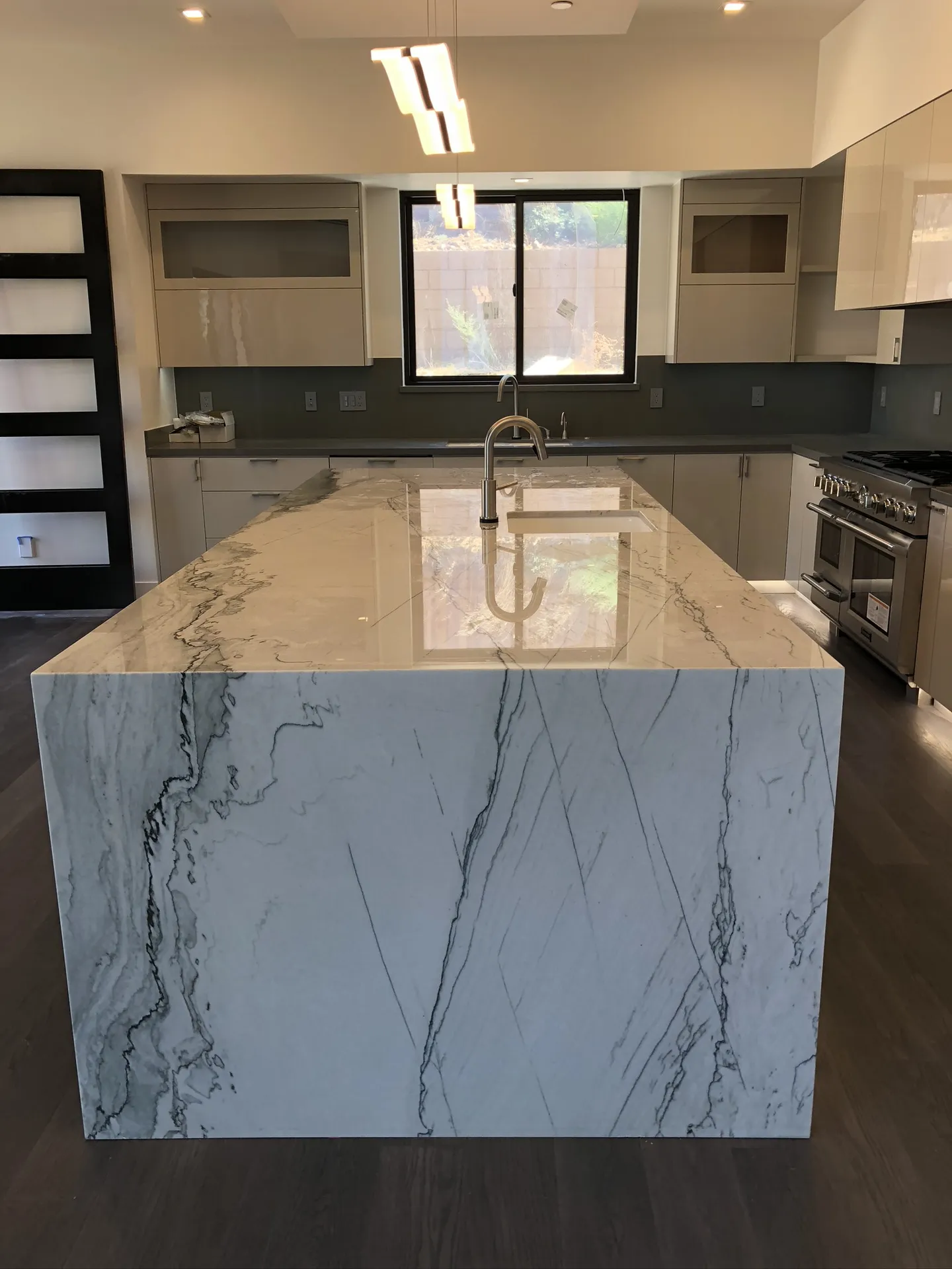 Modern kitchen remodel with white upper cabinets, black island, and marble waterfall countertops